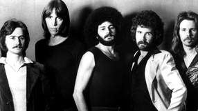 Pięciu mężczyzn w różnych stylach fryzur i ubioru, pozujących na tle w jednolitym kolorze.