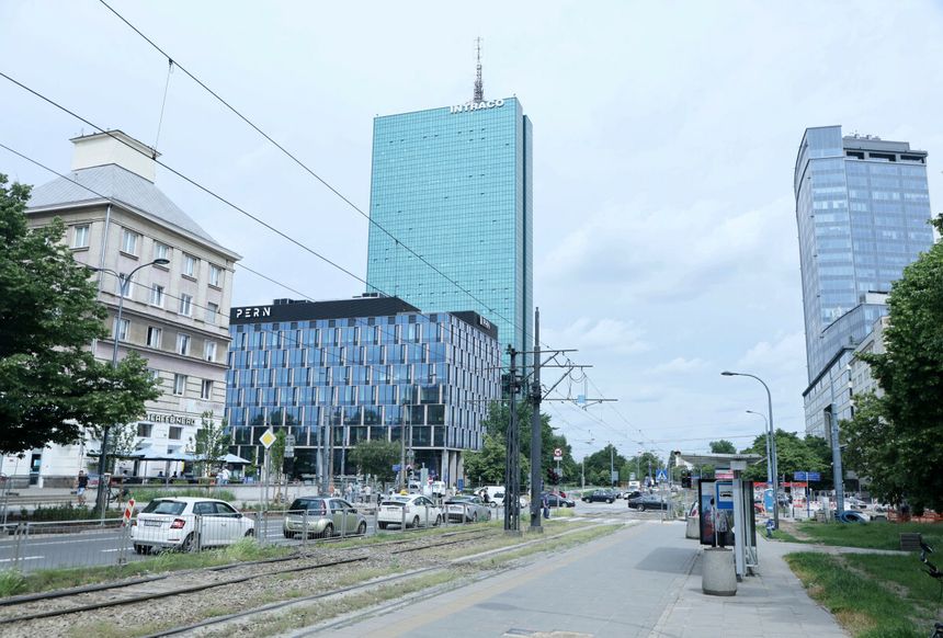 Nowoczesne budynki w mieście, w tle chmurne niebo, ruch uliczny na pierwszym planie.