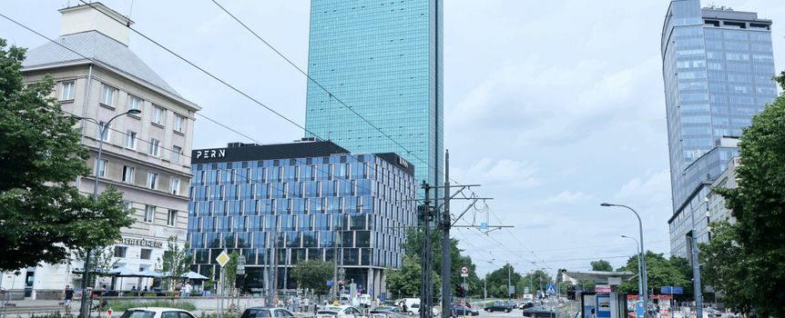 Nowoczesne budynki w mieście, w tle chmurne niebo, ruch uliczny na pierwszym planie.