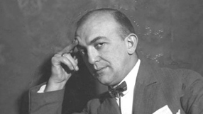 Jerzy Petersburski w eleganckim garniturze z muszką, dotyka czoła, myśli. Zdjęcie w czarno-białych tonach.