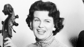 Uśmiechnięta Maria Koterbska z krótkimi, kręconymi włosami, w tle rozmyte postacie.