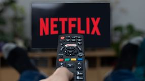 Pilot do telewizora z logo Netflix na ekranie, nogi w ciemnych skarpetach w tle.