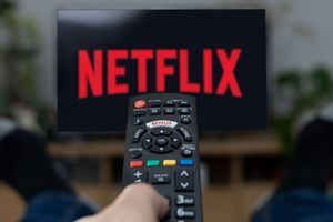 Pilot do telewizora z logo Netflix na ekranie, nogi w ciemnych skarpetach w tle.