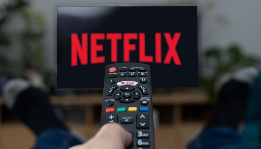 Pilot do telewizora z logo Netflix na ekranie, nogi w ciemnych skarpetach w tle.