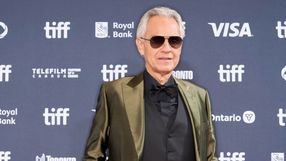 Mężczyzna w okularach przeciwsłonecznych w eleganckim garniturze, tło z logami festiwalu.