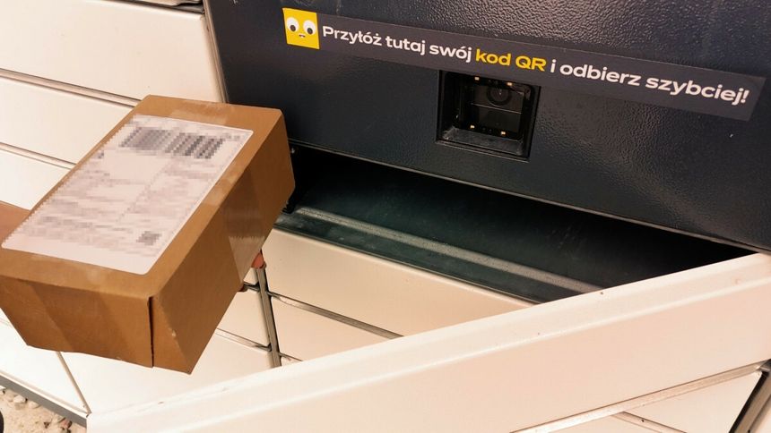 Osoba trzyma paczkę, zbliżając ją do skanera kodu QR przy samodzielnym punkcie odbioru.
