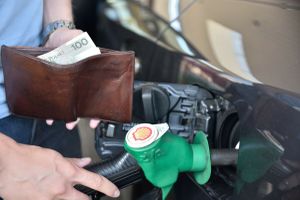 Mężczyzna tankuje samochód paliwem, trzymając w ręku portfel z banknotem 100 zł.