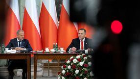 Donald Tusk, Karol Nawrocki przy stole, za nimi polskie flagi. U dołu bukiet z czerwonych i białych róż.