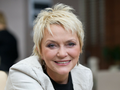 Małgorzata Ostrowska z krótkimi blond włosami, uśmiechająca się w jasnym otoczeniu.