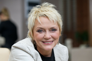 Małgorzata Ostrowska z krótkimi blond włosami, uśmiechająca się w jasnym otoczeniu.