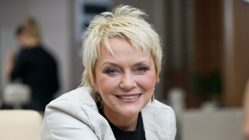 Małgorzata Ostrowska z krótkimi blond włosami, uśmiechająca się w jasnym otoczeniu.