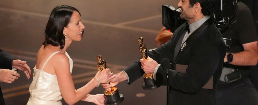 Dwie osoby w eleganckich strojach wymieniają się statuetkami oscarowymi na scenie.