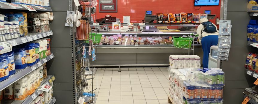 Zdjęcie przedstawia wnętrze sklepu spożywczego z regałami i ladą ze wędlinami.