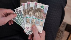 Osoba trzyma kilka polskich banknotów o różnych nominałach w dłoni.
