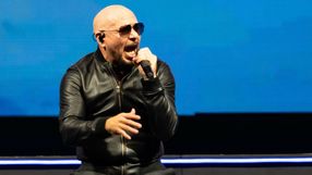 Na scenie występuje mężczyzna w czarnej kurtce, śpiewający i trzymający mikrofon.