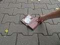 Ręka trzyma brązowy portfel leżący na chodniku, widoczne banknoty.