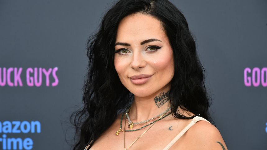 Na zdjęciu Sylwia Szostak z ciemnymi, kręconymi włosami, uśmiecha się, nosząc biżuterię.