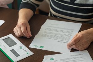 Na zdjęciu widać ręce osoby trzymającej dokumenty i kopertę z logo ZUS na drewnianym stole.