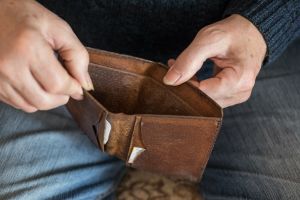 Ręka trzyma otwarty, zużyty portfel. Wnętrze pustego portfela. Tło zjeżdżającego dywanu.