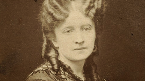 Kobieta z długimi, kręconymi włosami w XIX-wiecznym stroju, poważnym wyrazie twarzy.