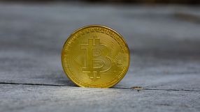 Złota moneta bitcoin na szarym tle, prezentująca symbol cyfrowej waluty.