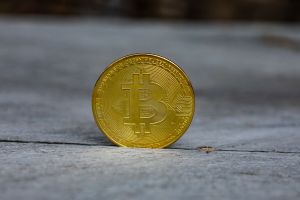 Złota moneta bitcoin na szarym tle, prezentująca symbol cyfrowej waluty.