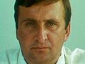 Zdjęcie mężczyzny o krótkich, ciemnych włosach, patrzącego w kamerę, z neutralnym wyrazem twarzy.
