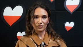 Na zdjęciu młoda kobieta w beżowej kurtce, z tłem w czerwono-białe serca.