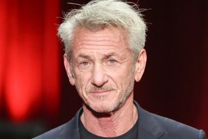 Mężczyzna w czarnym ubraniu z siwymi włosami i brodą, na tle czerwonych światł.