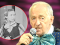 Andrzej Rosiewicz z mikrofonem, w kolorowym ubraniu, na scenie. W tle zdjęcie sprzed lat.