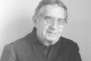 Czarnobiałe zdjęcie starszego mężczyzny (ksiądz Jan Twardowski) w okularach, z delikatnym uśmiechem.