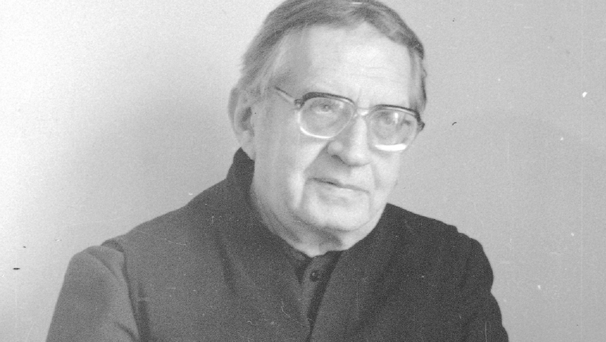 Czarnobiałe zdjęcie starszego mężczyzny (ksiądz Jan Twardowski) w okularach, z delikatnym uśmiechem.