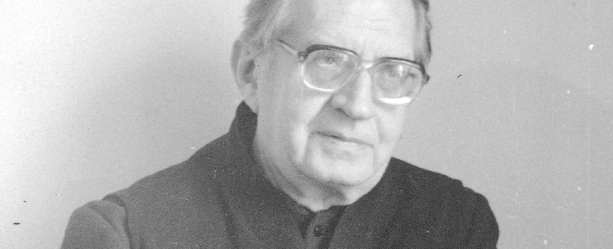 Czarnobiałe zdjęcie starszego mężczyzny (ksiądz Jan Twardowski) w okularach, z delikatnym uśmiechem.