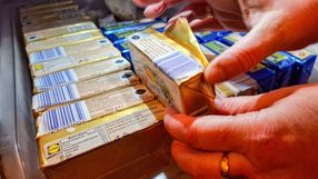 Ręce osoby wyjmującej produkty mleczne z lodówki, w tle opakowania w różnych kolorach.