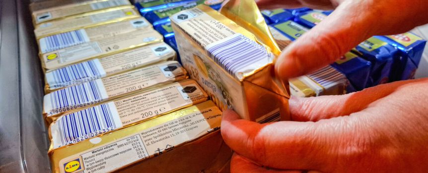 Ręce osoby wyjmującej produkty mleczne z lodówki, w tle opakowania w różnych kolorach.