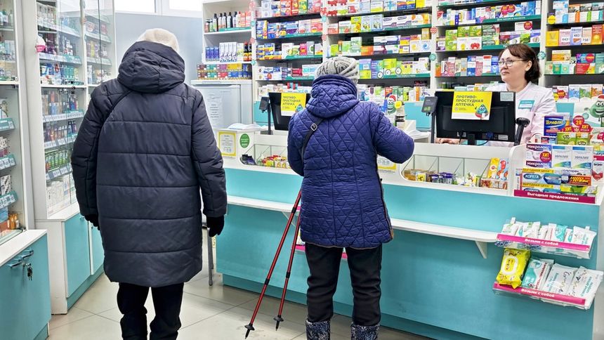 Zdjęcie przedstawia klientów apteki przy ladzie, obok pracownicy apteki. W tle regały z lekami.