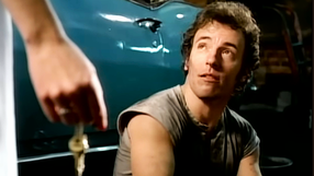 Na zdjęciu mężczyzna z krótkimi włosami, w szarej koszulce, patrzy na osobę trzymającą klucze.