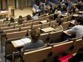 Spotkanie w sali wykładowej, prelegent przy stole, słuchacze siedzą na widowni.