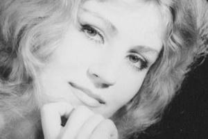 Anna German z falującymi włosami, przygląda się z uśmiechem, ręka przy twarzy. Czarno-biały portret.