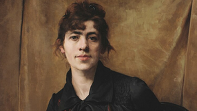 Portret młodej kobiety z brązowym tłem, w czarnej sukience, z delikatnym uśmiechem.