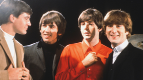 Muzycy z zespołu The Beatles w modnych strojach lat 60. uśmiechających się do siebie.