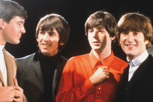 Muzycy z zespołu The Beatles w modnych strojach lat 60. uśmiechających się do siebie.