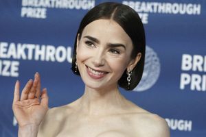 Na zdjęciu uśmiechająca się kobieta z krótkimi warkoczami, w eleganckiej sukni, na niebieskim tle.