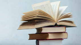 Stos książek, na wierzchu otwarta książka ze stronami przewracającymi się do przodu.