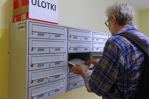 Mężczyzna sprawdza pocztę w skrzynce na ulotki w budynku mieszkalnym.