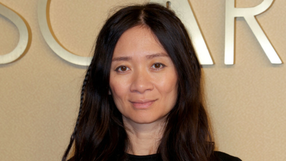 Na zdjęciu portret Chloé Zhao z długimi, ciemnymi włosami, uśmiechającej się lekko.