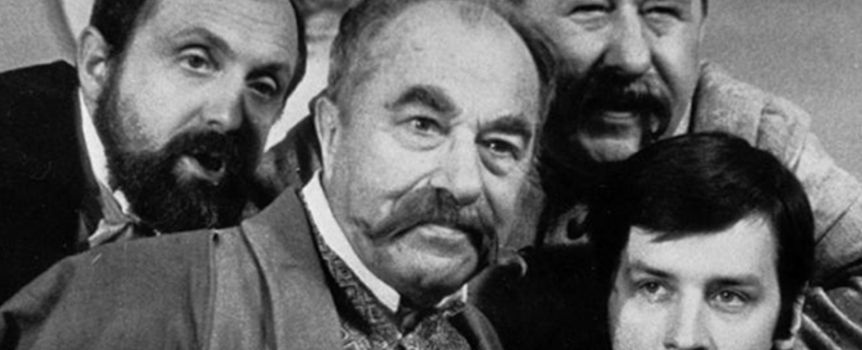 Czterech mężczyzn w tradycyjnych strojach z zaczesanymi brodami i poważnymi wyrazami twarzy.