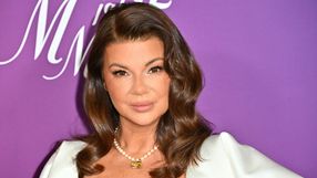 Kobieta z brązowymi włosami, uśmiechająca się, na tle fioletowego tła. Elegancka stylizacja.