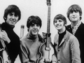 Muzycy z The Beatles z gitarami, uśmiechniętych, pozujących do zdjęcia w czarno-białej tonacji.