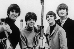 Muzycy z The Beatles z gitarami, uśmiechniętych, pozujących do zdjęcia w czarno-białej tonacji.